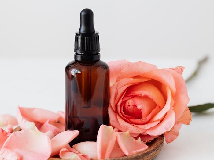 Elegant dropper bottle with pink rose petals on a wooden plate, perfect for aromatherapy or skincare.